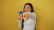 © Krakenimages.com - Woman holding credit card and pointing excitedly against a vibrant yellow background, showcasing financial confidence and modern lifestyle with a cheerful expression