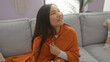 © Krakenimages.com - Woman sitting indoors in cozy apartment wrapped in orange blanket smiling relaxed on comfortable sofa in bright living room