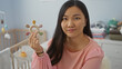© Krakenimages.com - Young asian woman smiling in a baby room holding a toy, surrounded by a cozy home interior, symbolizing family and warmth.