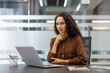 © Liubomir - A thoughtful businesswoman works on her laptop in a modern office setting, considering a project's details.