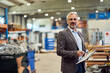 © bnenin - Confident Businessman Standing in Modern Industrial Warehouse Holding Paperwork