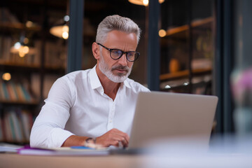 Poster - A man wearing glasses is typing on a laptop computer