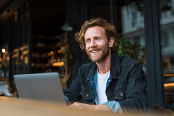 Poster - A man with a beard and a smile is sitting at a table with a laptop