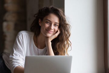 Poster - A woman with long hair is sitting in front of a laptop, smiling