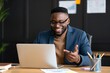© MH - Young Black professional man smiles while working on a laptop at his desk in a modern office setting, collaborating effectively.