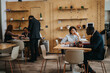 © qunica.com - Professionals seated around tables, engaging in dialogues and brainstorming ideas in a modern, well-lit co working environment with wood panel decor.