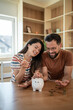 © Migma_Agency - Happy couple saving money together in piggy bank at home