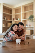 © Migma_Agency - Happy couple saving money together in piggy bank at home