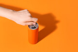 Female hand opening soda can on orange background