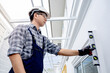 © Summer Paradive - Asian male construction worker using level tool while installing the new window. Home builder man checking the vertical plane of house wall. Measuring tool for building measurement and inspection