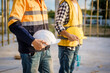 © NanSan - An elderly engineer and a middle-aged man at a construction site engage in a serious discussion one placing  shoulder, symbolizing guidance, mentorship, and on-site professional collaboration