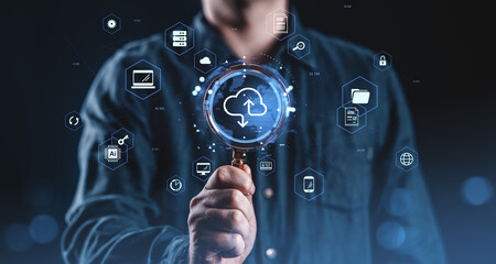 Fototapete - Man holding magnifying glass over cloud computing icon with futuristic digital interface and data technology symbols on dark blue background concept..