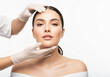 © PictoAi - A woman with smooth, clear skin and dark hair pulled back is positioned against a white background. A gloved hand gently holds her chin, suggesting a cosmetic treatment or consultation