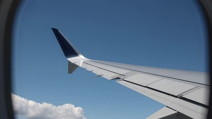 Aufkleber - Passenger airplane wing stretching across vibrant blue sky, white fluffy clouds drifting beyond aircraft window, capturing serene aerial journey and expansive panoramic landscape
