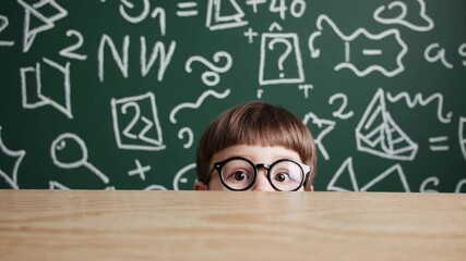Aufkleber - Schoolboy with eyeglasses peeks over school desk in front of green chalkboard with math equations and drawings, expressing curiosity and playfulness in educational setting