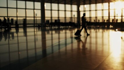 Poster - Warm sunlight illuminates the airport terminal as a businessman walks with his rolling suitcase, creating a long shadow on the polished floor