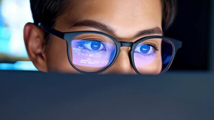 Eyes of a woman wearing glasses reflecting a computer screen with lines of code, focused on work, illuminated by blue light.