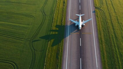 Aufkleber - Passenger white airplane slowly taxiing across green grass runway, casting long shadow while preparing for imminent departure, showcasing aviation transportation sequence