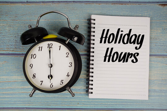 Holiday Hours text written on notepad with alarm clock on wooden background