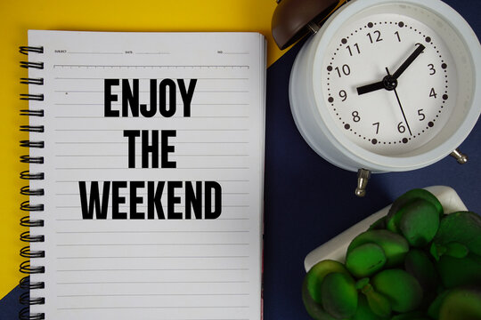 Enjoy The Weekend text written on notepad with alarm clock on blue background