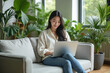 © Sync - Woman using laptop surrounded by plants, bright cafe indoor working space