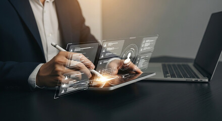 Poster - Man using a tablet with a stylus and a holographic interface next to a laptop on a dark surface