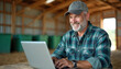 © Pete - Smiling senior farmer using laptop in barn. Happy agricultural worker, rural business owner, planning harvest. Agriculture tech, farmland, positive attitude, eco-friendly farm. Man work, internet.