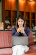 © Satori Studio - A woman in a cafe enjoying a cup of coffee while working on her laptop, surrounded by a warm wooden interior.