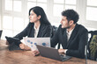 © Rakchanok - Caucasian Hispanic man discussing work with woman at office desk. male and female working together. Business interaction, teamwork, or small business couple strategic planning work at home office