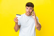 © luismolinero - Young caucasian handsome man isolated on yellow background keeping a conversation with the mobile phone and holding a credit card