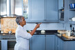© wavebreak3 - Senior Asian woman pointing at upper cabinet in modern kitchen with stainless steel kettle