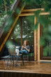 © boomeart - Pretty woman reading in smartphone outside a modern wooden cabin