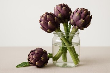 Poster - Vivid purple artichokes stored in a clear jar with a single flower nearby on a plain white surface, focus on distant blooms