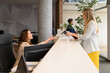 © Moon Safari - Side view of smiling businesswoman giving passport and document to receptionist at modern desk in office lobby