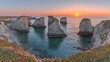 © arif - Coastal sunset panorama with dramatic rock formations.  Sunrise hues paint the sky over a tranquil bay, featuring several prominent, light-colored, craggy rocks rising from the water.