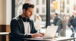 © Danmoch - Young Man Focused on Working with Laptop in CafeA young brown-haired man with headphones around his neck looks intently at his laptop screen while typing, sitting by a bright cafe window.