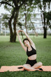 © Worawi - A young woman practices yoga outdoors in a peaceful urban park, promoting wellness, balance, and mindfulness through stretching exercises on a mat surrounded by nature and tranquility.