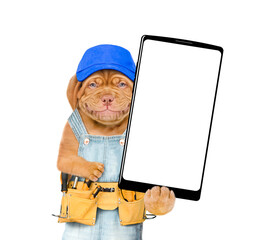 Poster - Smiling Mastiff puppy wearing blue cap and overalls with tool belt showing big smartphone with white blank screen in it paw. Isolated on white background