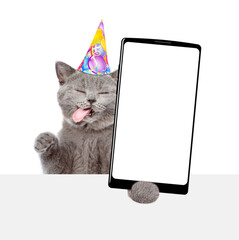 Poster - Happy licking lips cat wearing party cap shows big smartphone with blank screen above blank white banner. Empty free space for text. isolated on white background