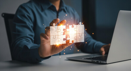 Poster - Person holding together puzzle pieces with laptop in the background on a white surface