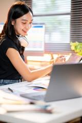 Fototapete - Asian woman designer drawing on tablet looking at color chart while sit with laptop at working table