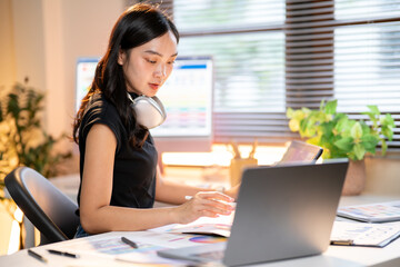 Fototapete - Asian woman designer holding stylus looking at color chart sit with laptop at office's working table
