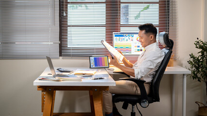 Fototapete - Asian man designer holding looking at clipboard over color chart and laptop at office working table.
