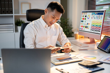 Fototapete - Asian man designer looking at chart choosing color to use while sitting at office's working table.