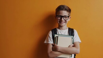 Poster - Confident schoolboy wearing backpack and eyeglasses, standing with textbooks and radiating joy while posing against vibrant orange background, representing academic enthusiasm