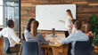 © Monkey Business - Young Businesswoman In Front Of Whiteboard Making Presentation To Colleagues Around Table In Office