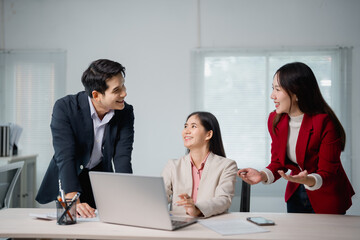 Poster - Three Asian businesspeople engaging in a strategy discussion while collaborating on a project, using a laptop in a modern office, smiling and fostering teamwork for success
