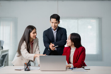 Fototapete - Three asian businesspeople are discussing work, using a laptop in a modern office, collaborating on a project and sharing ideas in a dynamic and productive environment