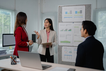 Aufkleber - Asian businesspeople engaging in a meeting, discussing marketing strategies while analyzing charts and graphs displayed on a whiteboard in a modern office environment