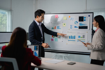 Aufkleber - Asian businessman in suit pointing at whiteboard presenting company strategy and showing marketing research results to colleagues in modern office